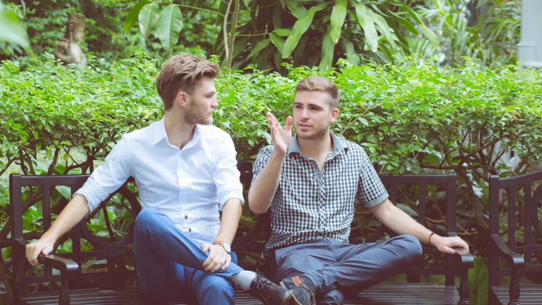 Two people sitting together in conversation, surrounded by greenery