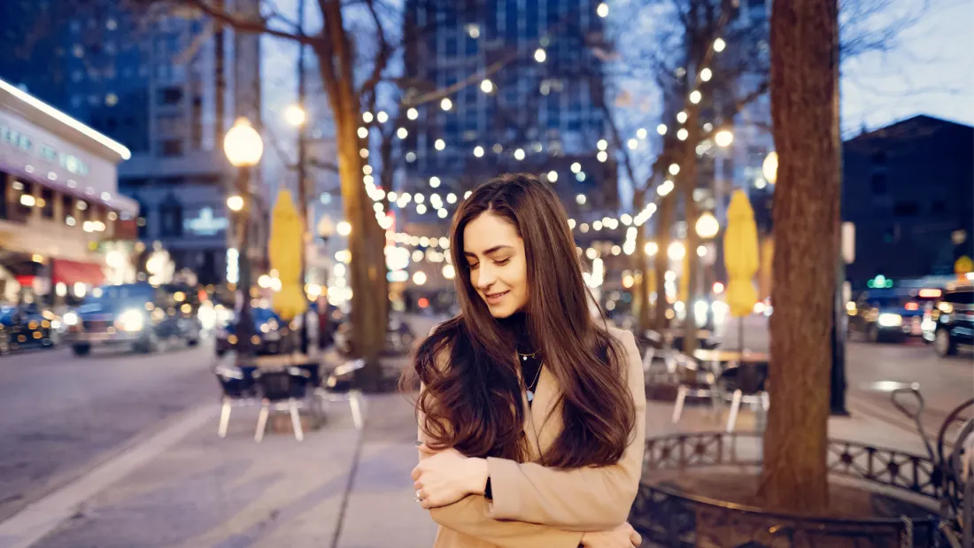 A woman standing calmly among warm evening lights